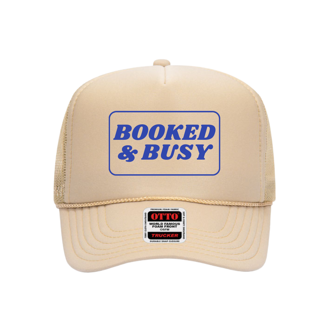 Beige trucker hat with 'Booked & Busy' text on a white background