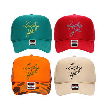 A collection of four custom trucker hats in different colors, each featuring the text 'Lucky You' embroidered on the front.
