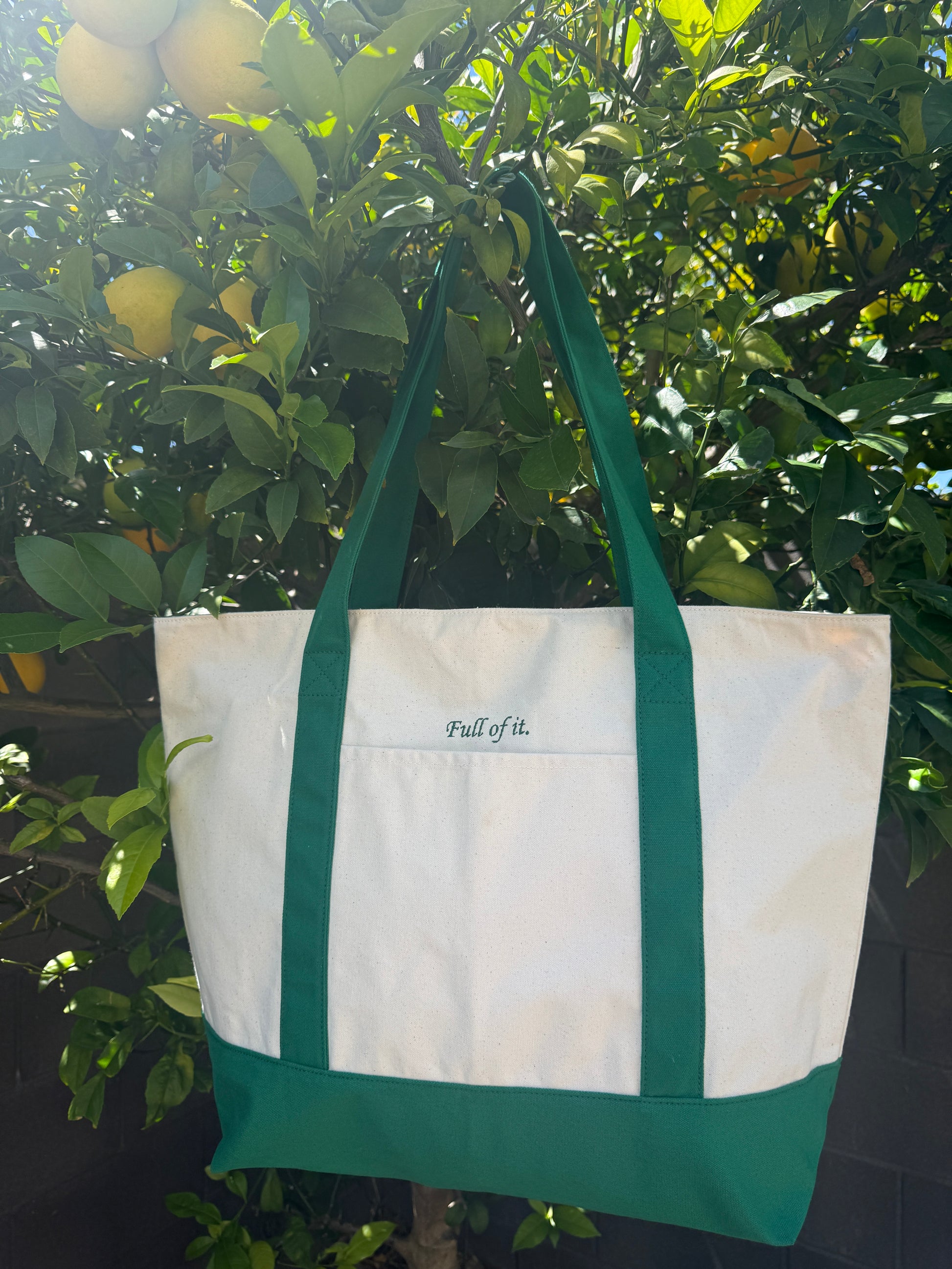 White tote bag with green handles hanging on a tree