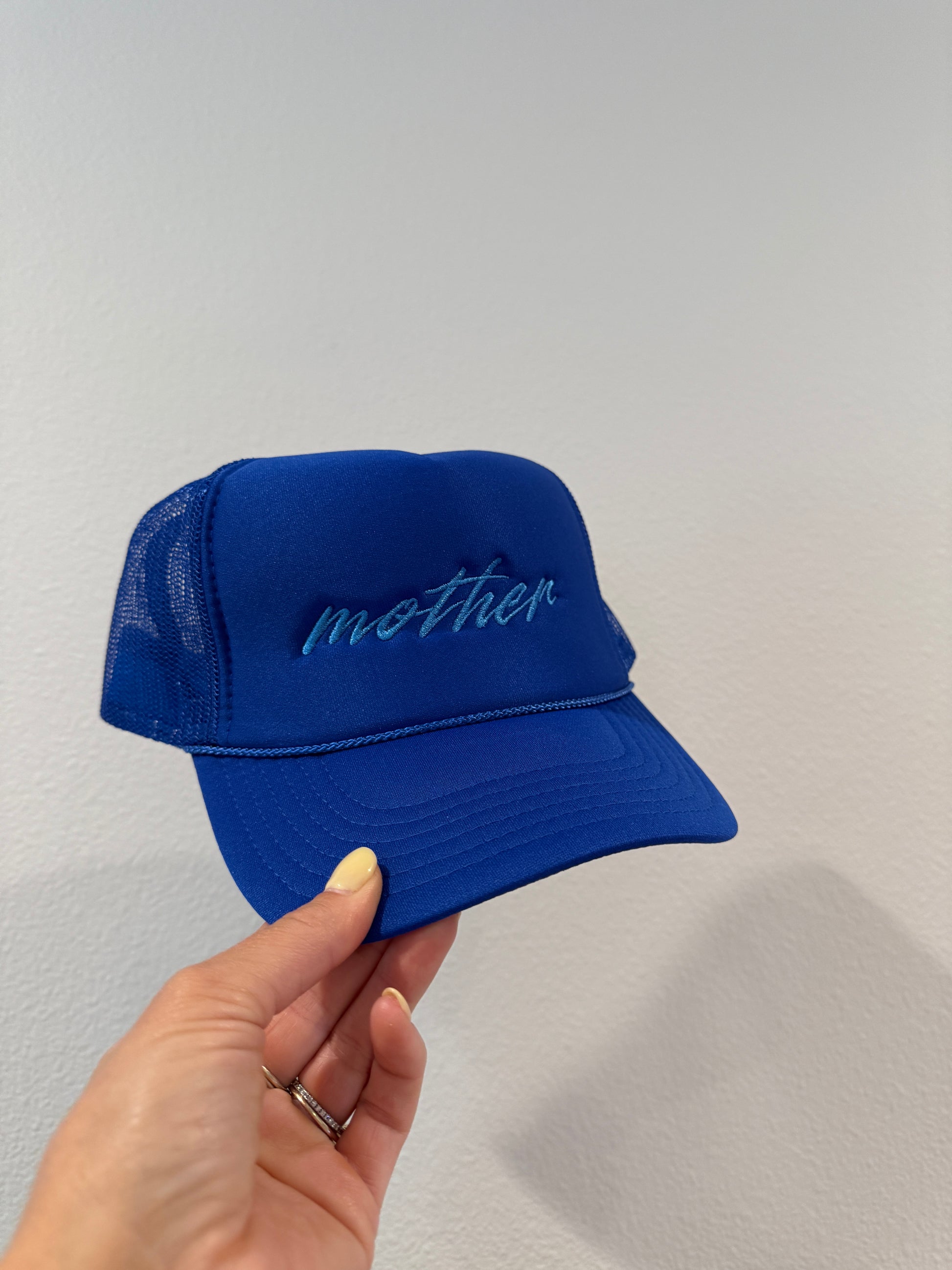 Blue trucker hat with "mother" embroidery held by a hand against a white background
