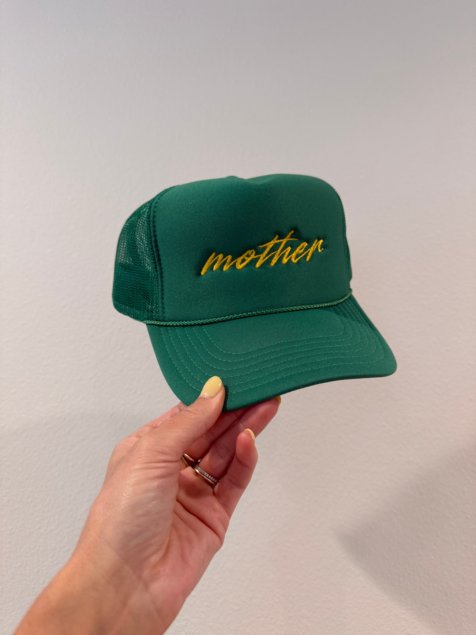 Green cap with yellow mother text held by a hand against a plain background