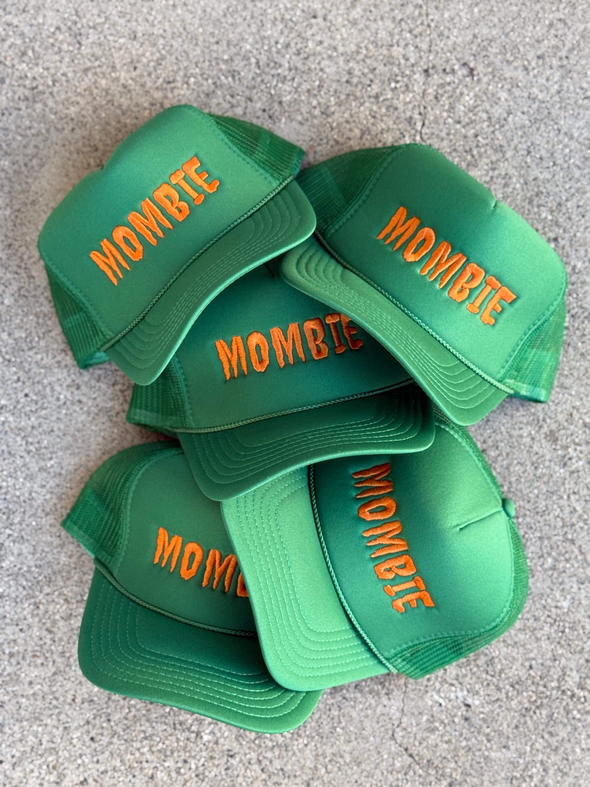 Stack of green caps with 'Mombie' text on a gray surface